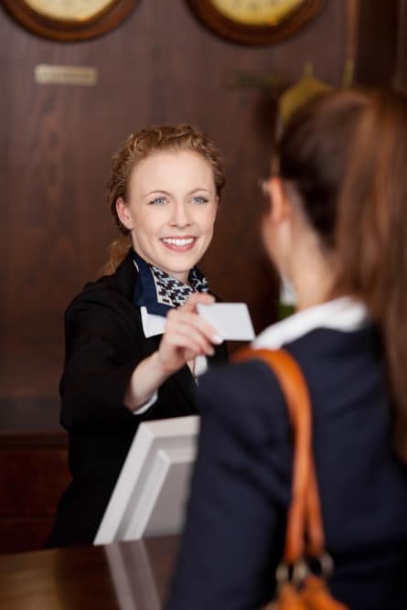 Hotel receptionist warmly greeting a guest, exemplifying excellent customer service in the hospitality industry that is supported by secure fax for hotels.